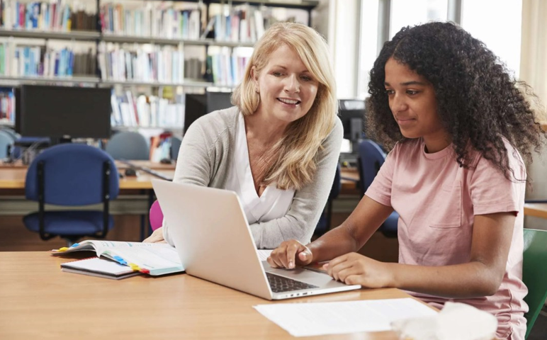 Teacher helping student on computer in library.