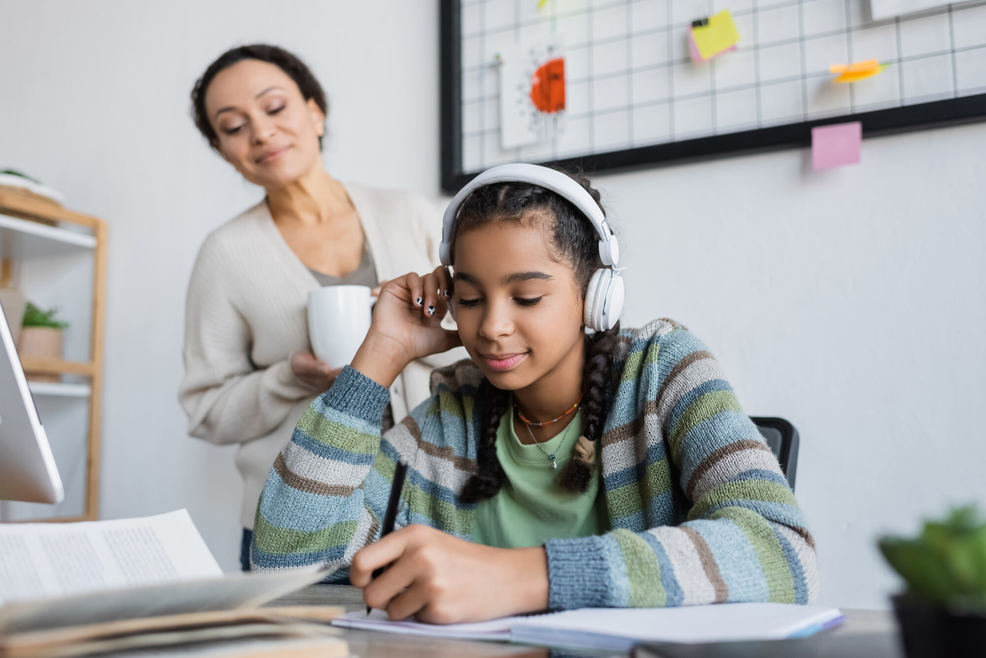 High school girl sitting at desk writing in notebook while mom looks over her shoulder.