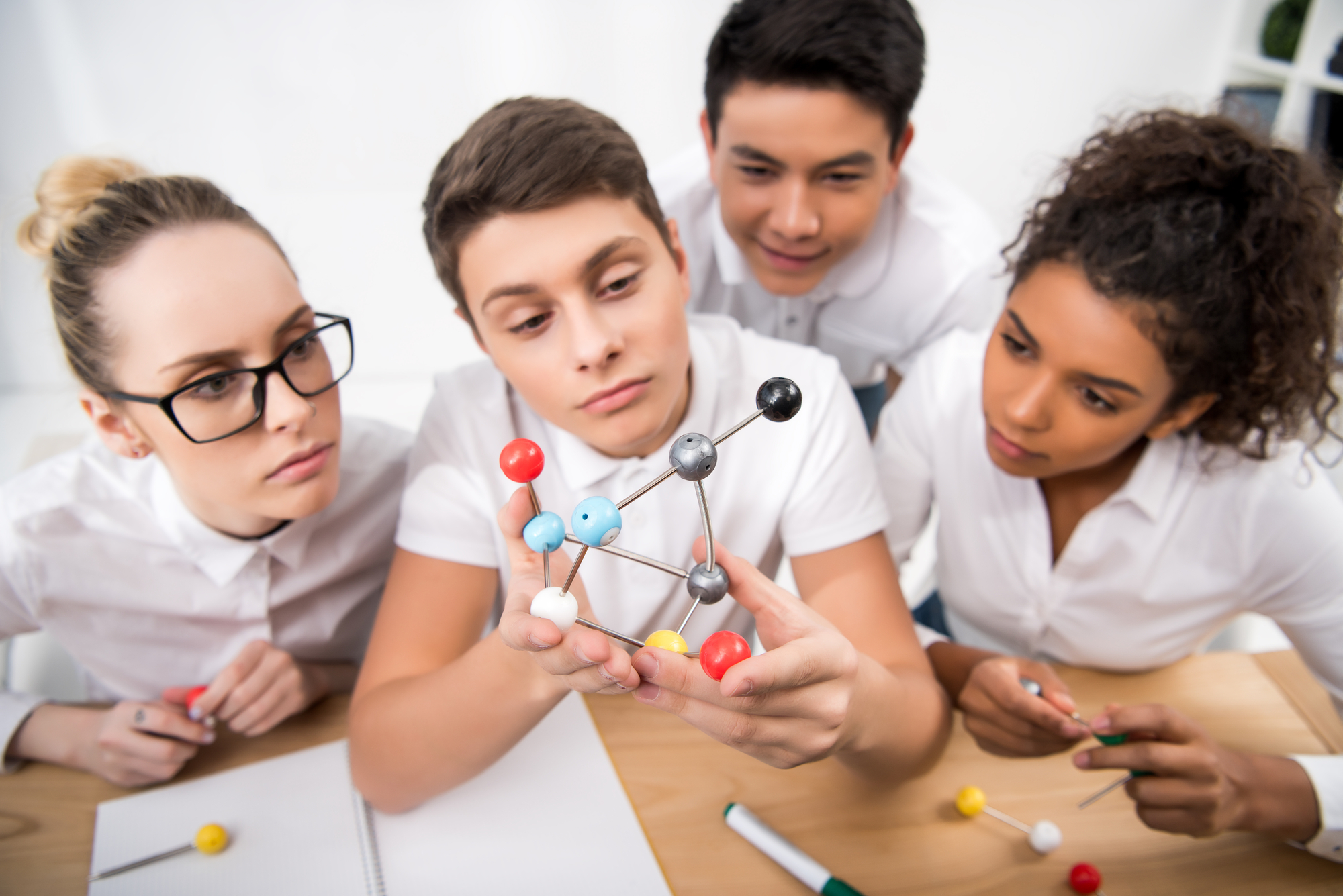 Four high school student looking at atom diagram in classroom.