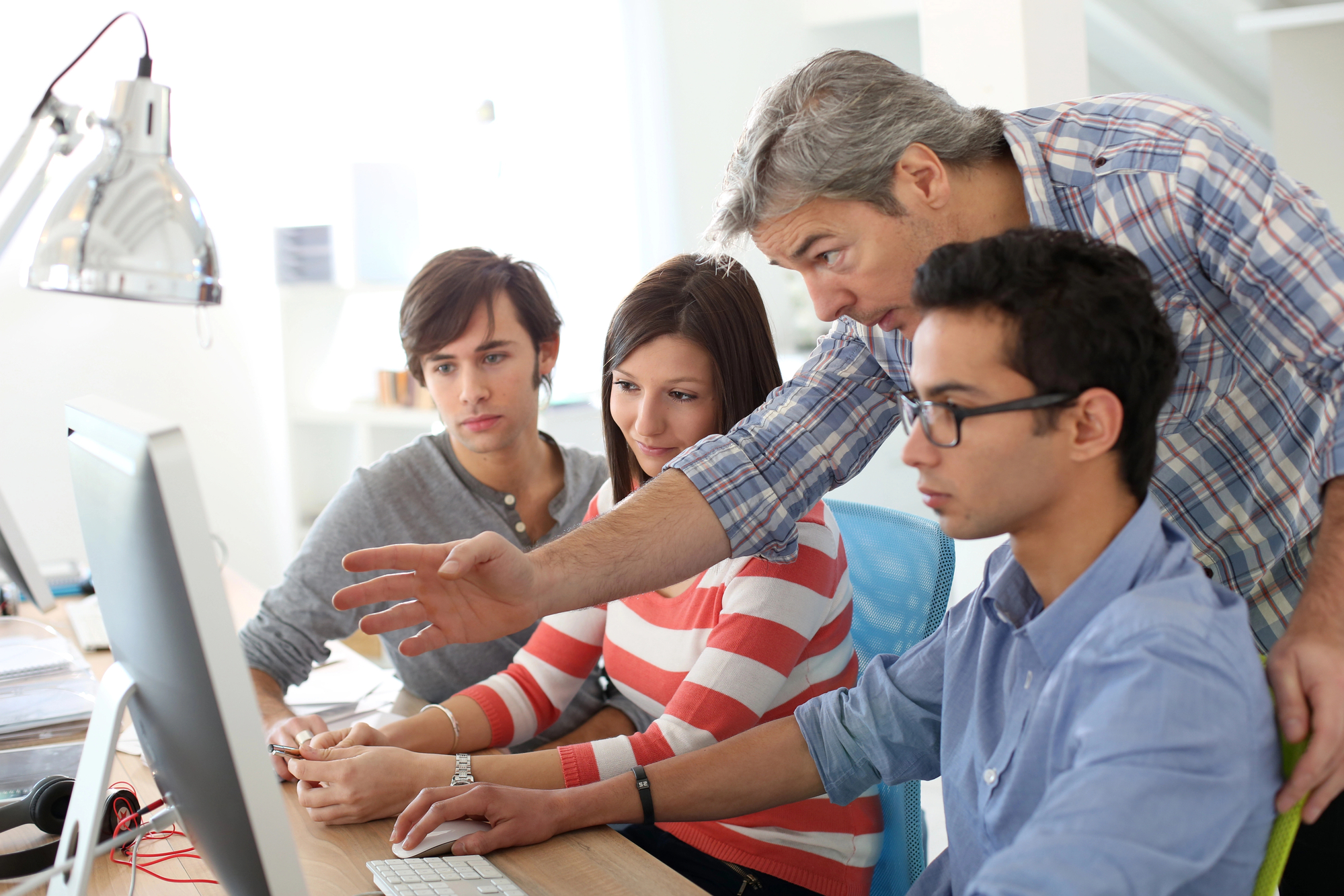 Three high school kids at computer with teacher helping them.