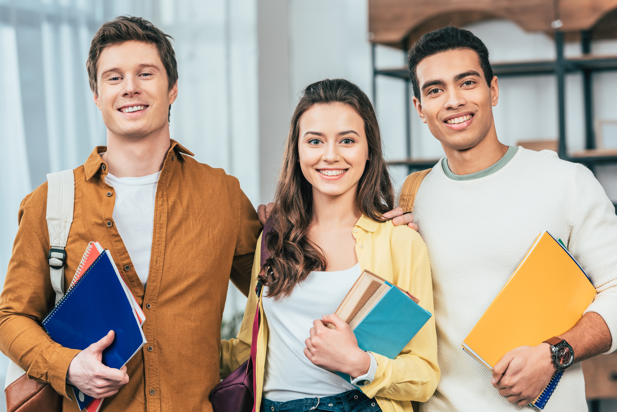 Three college students holding books.