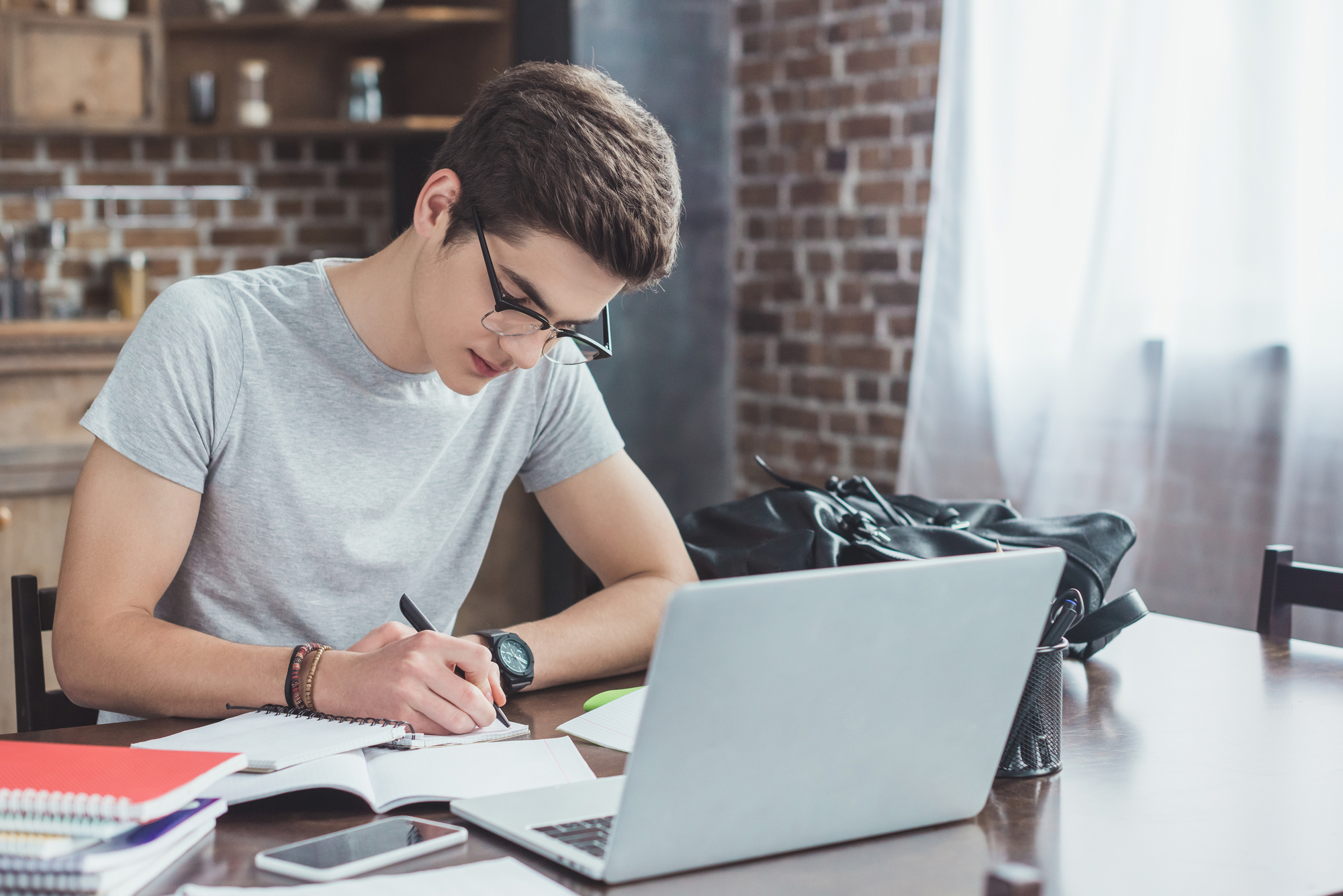 High School boy writing in a notebook while sitting at a desk.