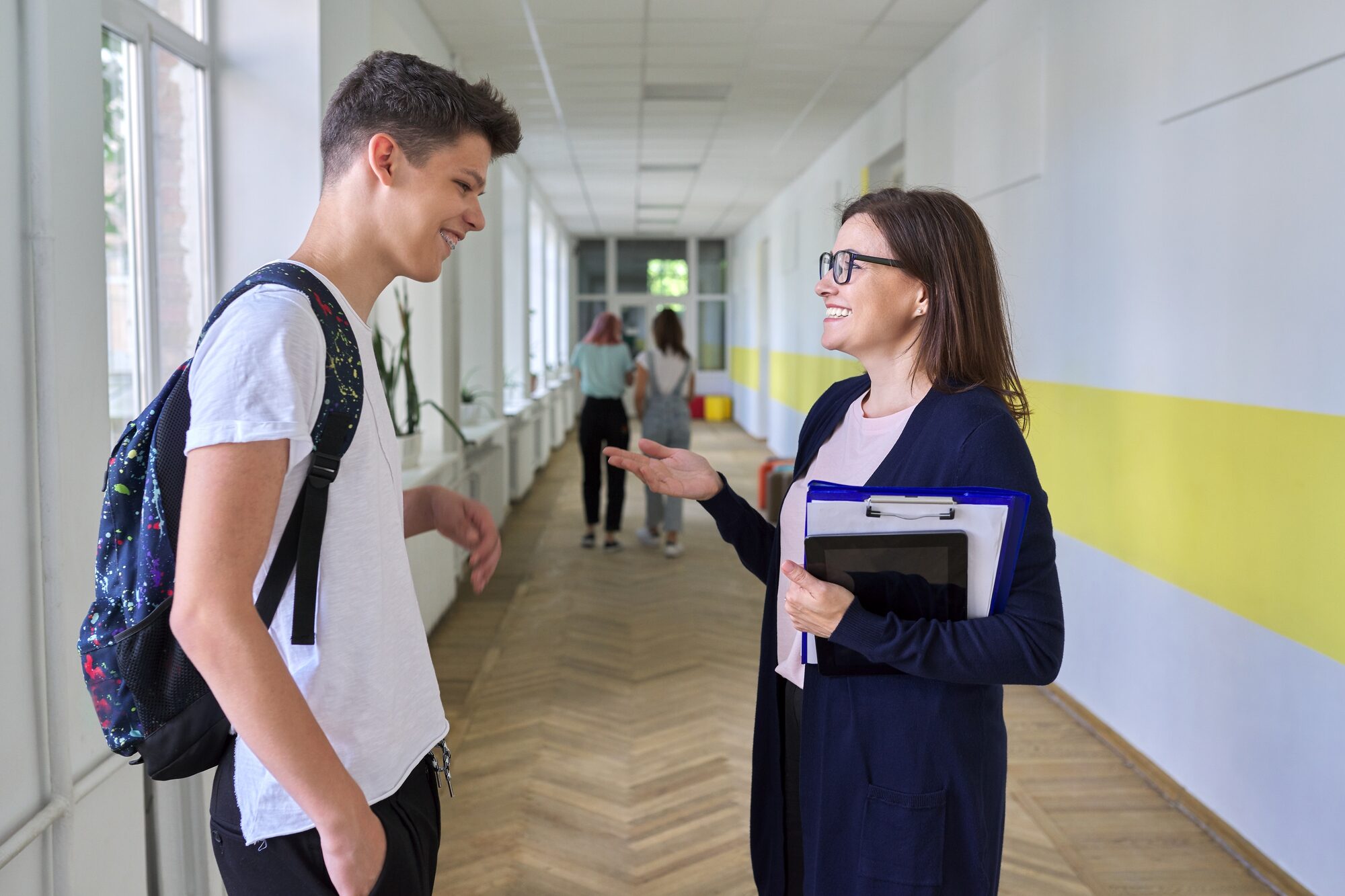Teacher talking to teen boy in hallway of school