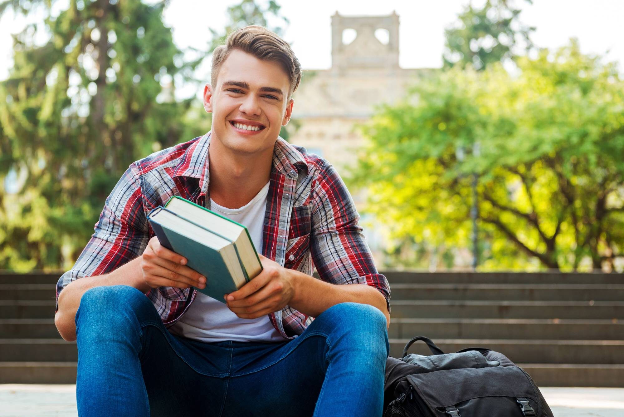 Teen boy sitting on a bench holding books.