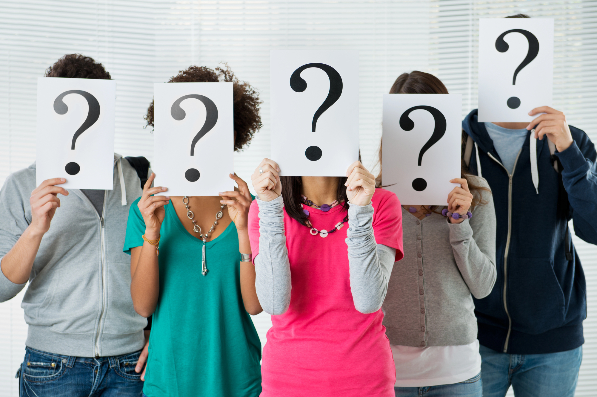 Group of teens holding question mark signs in front of their faces, symbolizing uncertainty about college planning.