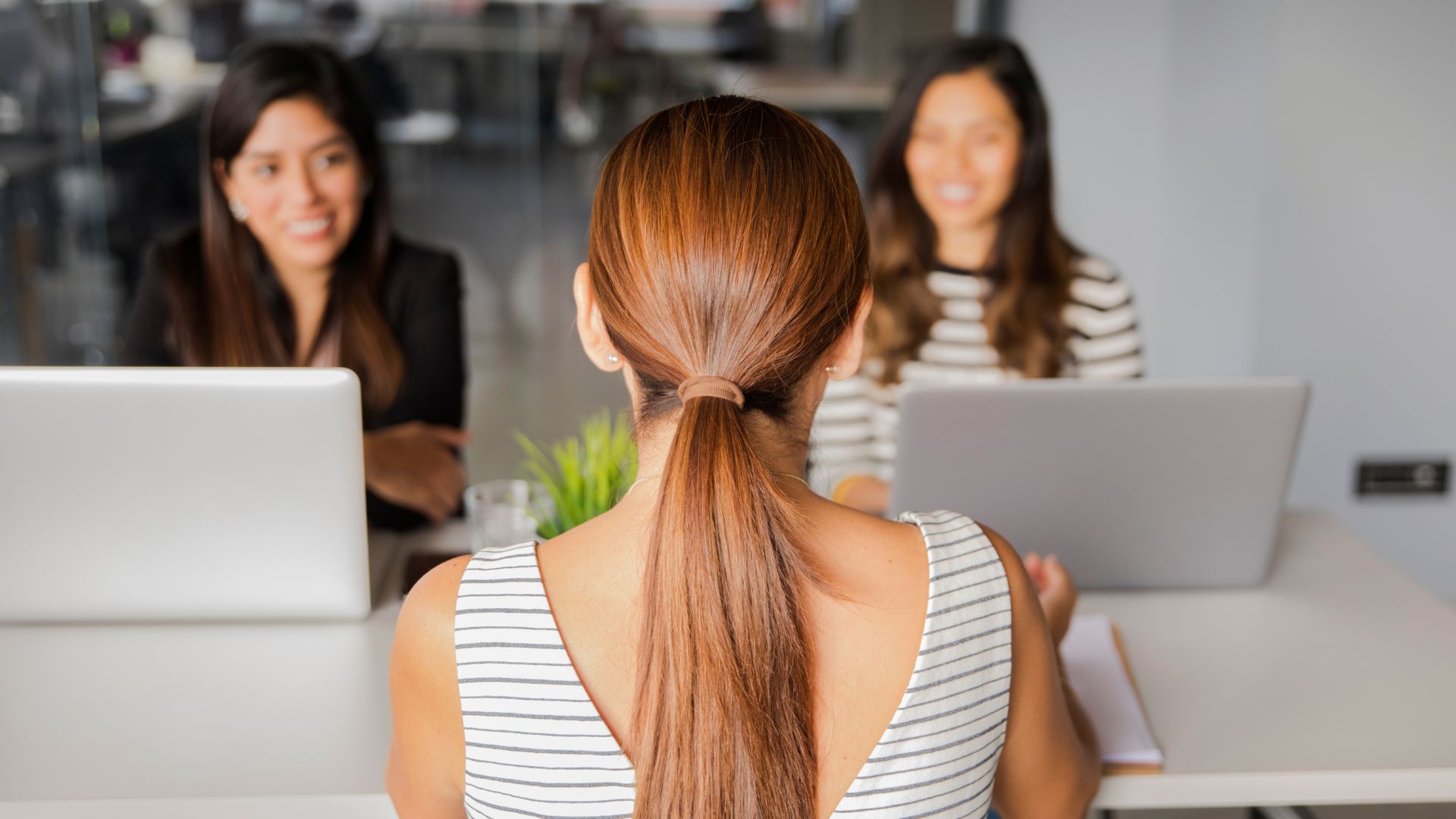 Teen sitting across from two professionals at a meeting table with laptops, representing networking and college or career readiness.