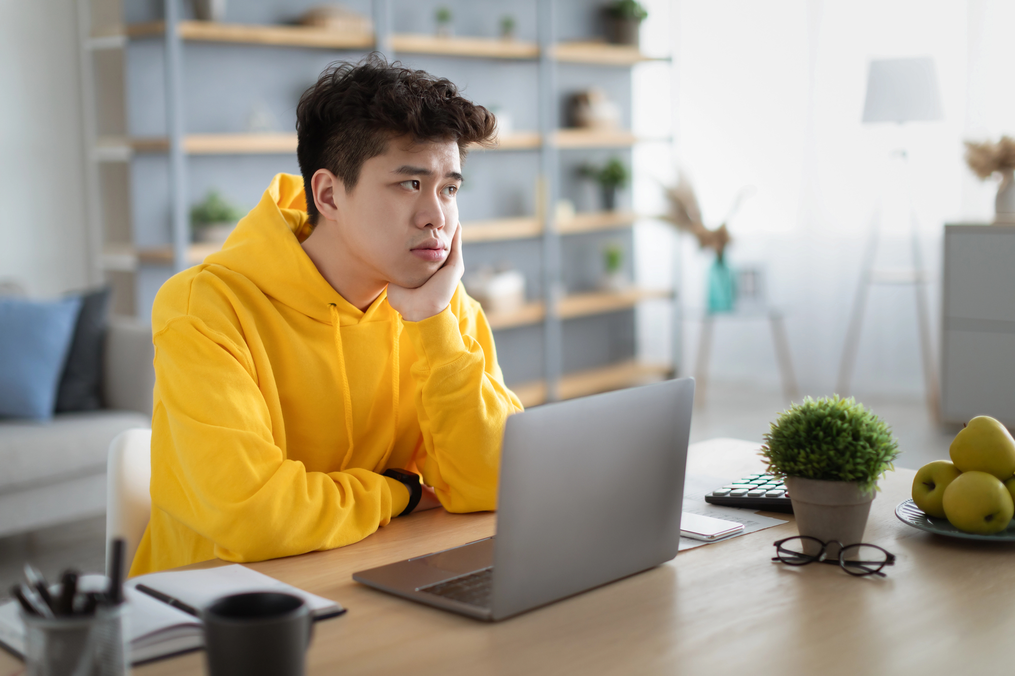 A tired high school student wearing a yellow hoodie sits at a desk with a laptop, looking stressed and overwhelmed—illustrating teen burnout during the busy fall school season.