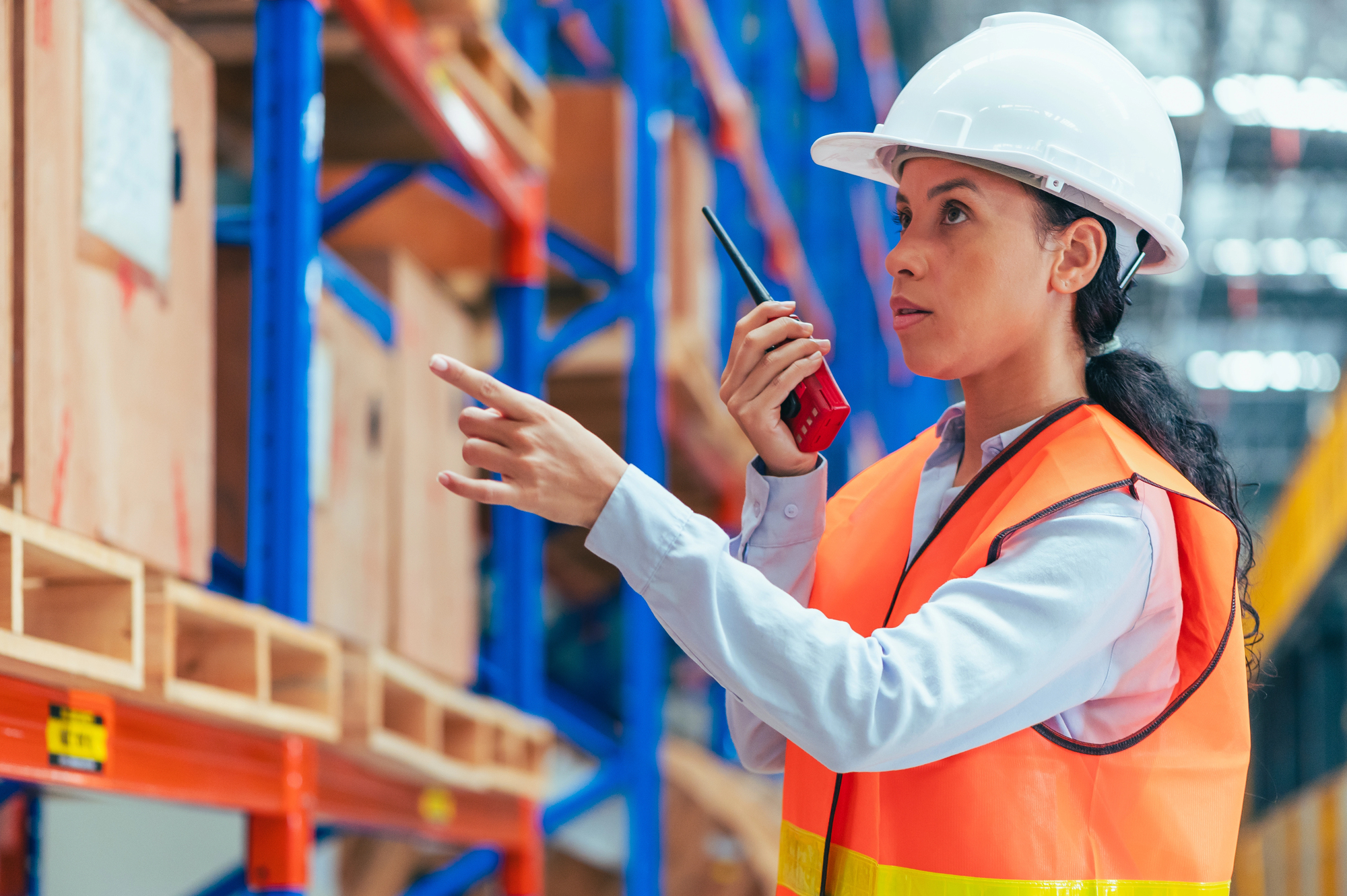 Young skilled trades professional wearing safety gear and using a radio in a modern warehouse environment
