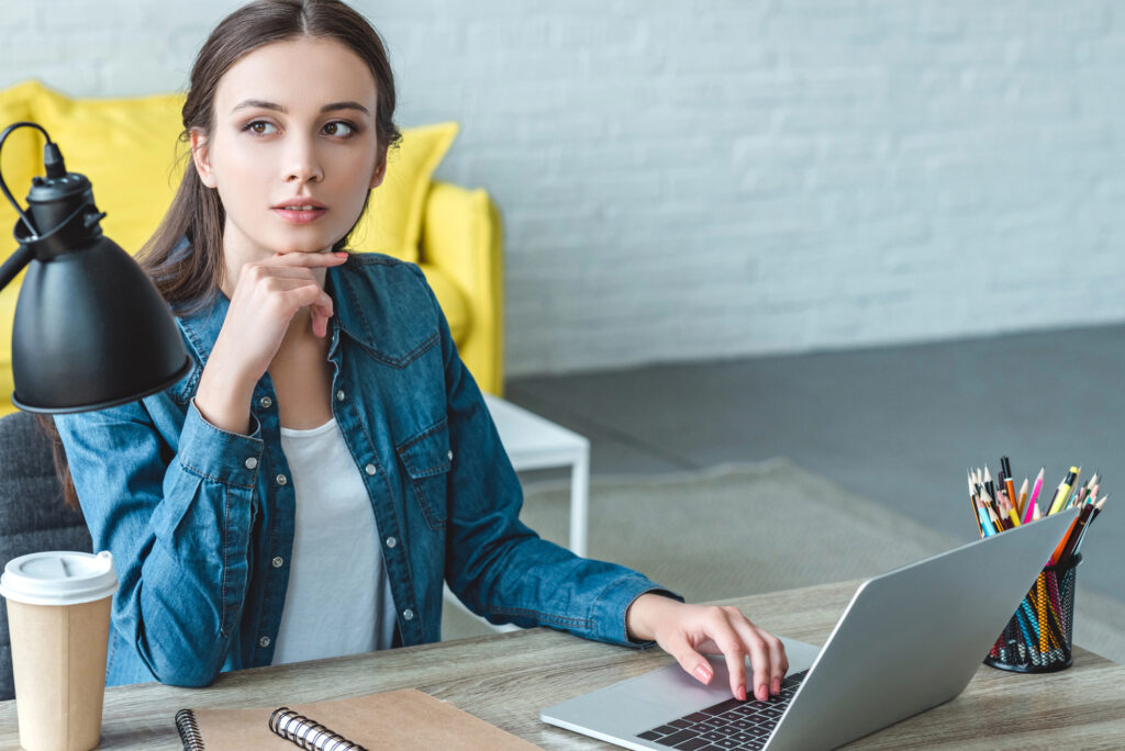 Teen girl sitting at a desk with a laptop, looking thoughtful in a home study space, representing future planning and direction.