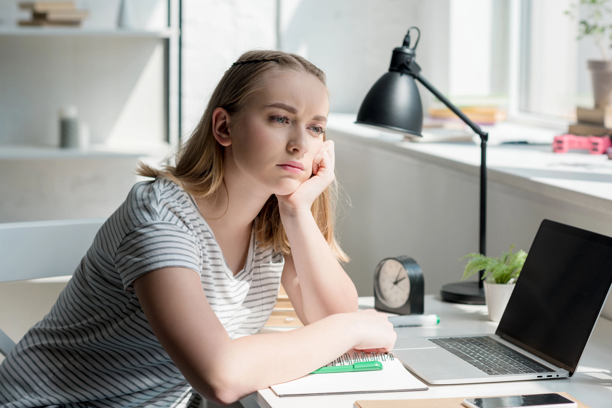 Teen girl sitting at a desk with a laptop and notebook, thinking about her future plans.