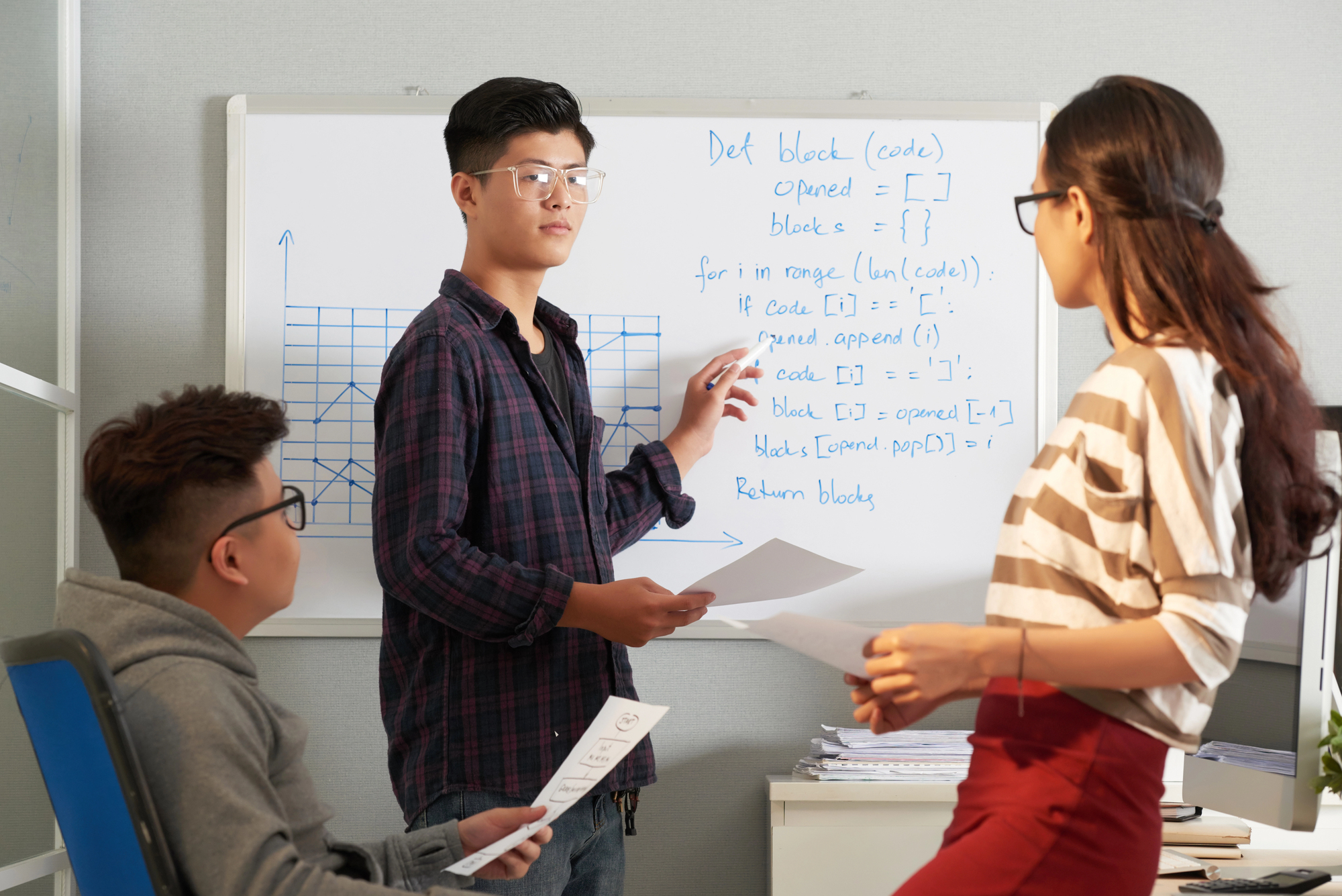 High school students collaborating during a classroom presentation in front of a whiteboard with charts and code.